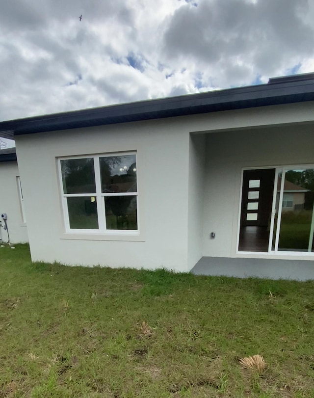 back of property with stucco siding and a yard