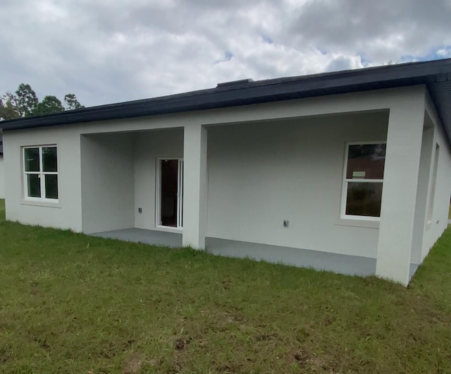 rear view of property featuring a lawn and stucco siding