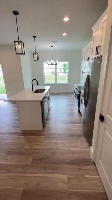 kitchen featuring decorative light fixtures, a kitchen island with sink, stainless steel appliances, white cabinetry, and a sink