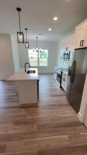 kitchen with a sink, white cabinetry, appliances with stainless steel finishes, light wood-type flooring, and an island with sink