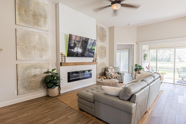 living area with a ceiling fan, a glass covered fireplace, baseboards, and wood finished floors