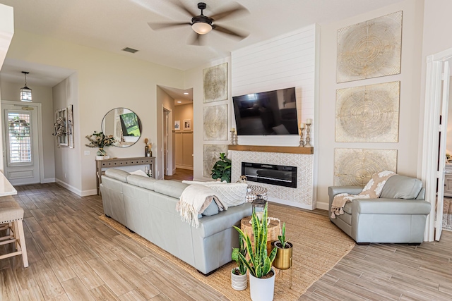 living room featuring a tile fireplace, a ceiling fan, visible vents, baseboards, and light wood-type flooring