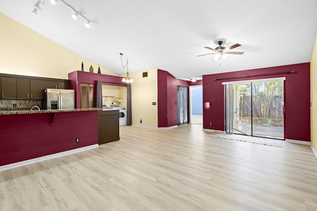 kitchen with a breakfast bar, stainless steel refrigerator with ice dispenser, washer / clothes dryer, vaulted ceiling, and a textured ceiling