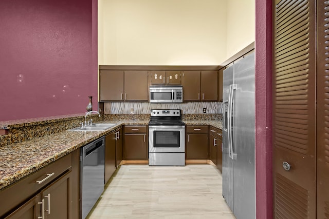 kitchen with dark stone counters, a towering ceiling, stainless steel appliances, light wood-style floors, and a sink