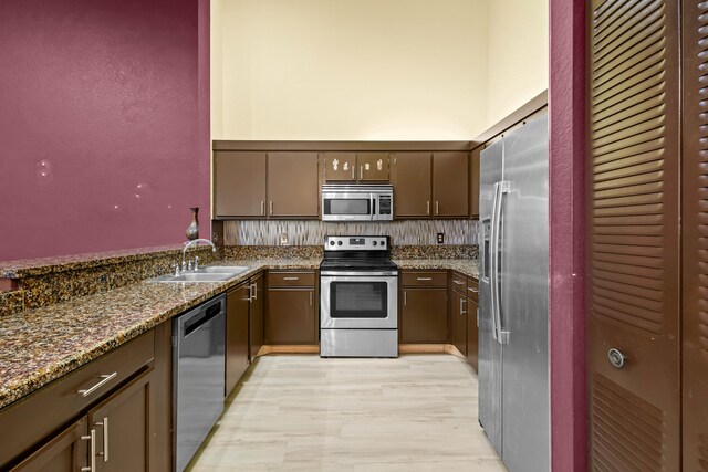 kitchen with light wood finished floors, appliances with stainless steel finishes, a sink, high vaulted ceiling, and a peninsula