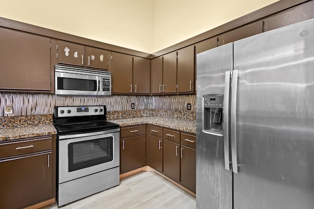 kitchen with dark brown cabinetry, light wood-style flooring, appliances with stainless steel finishes, and dark stone counters