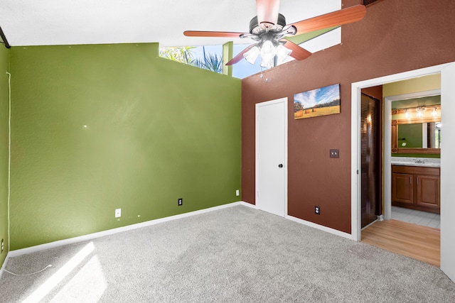 unfurnished bedroom featuring lofted ceiling, light carpet, connected bathroom, and baseboards