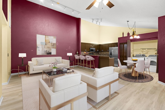 living area featuring light wood-style floors, high vaulted ceiling, separate washer and dryer, and ceiling fan with notable chandelier