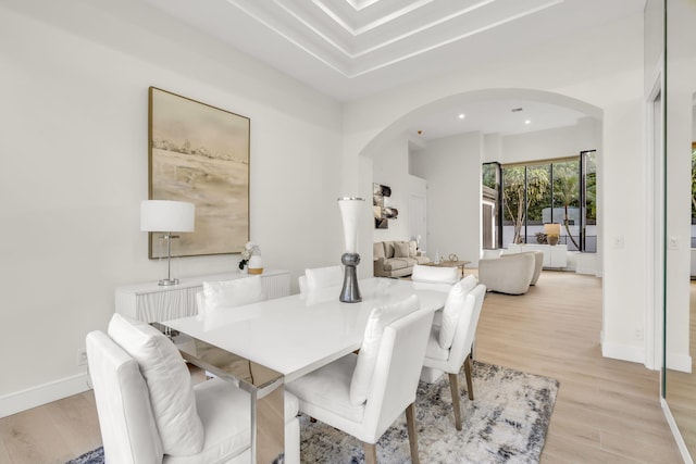 dining room featuring arched walkways, light wood-style flooring, and baseboards