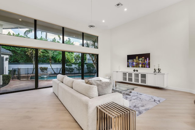 living area with visible vents, baseboards, recessed lighting, light wood-style floors, and a towering ceiling