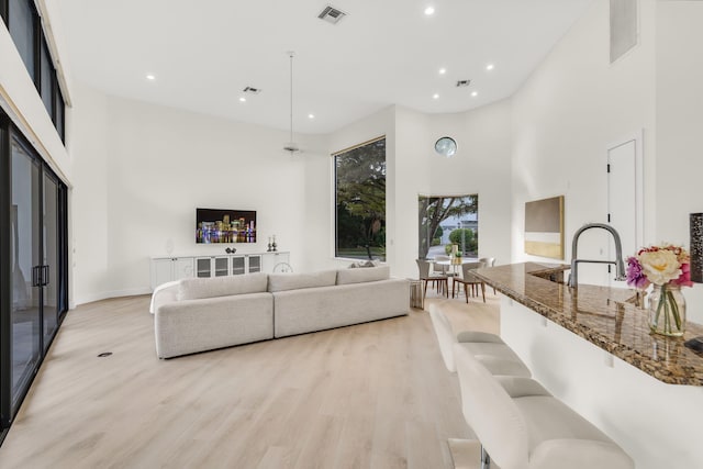 living area with recessed lighting, light wood-style floors, visible vents, and a towering ceiling