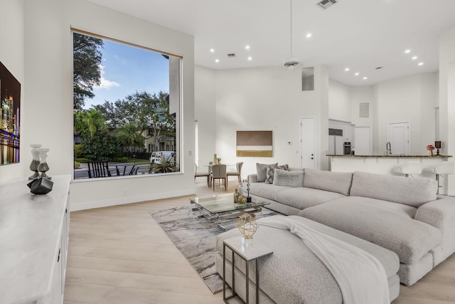 living area with visible vents, baseboards, recessed lighting, light wood-style floors, and a towering ceiling