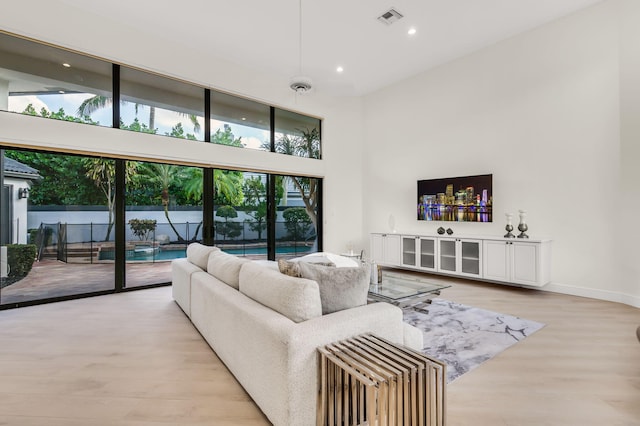 living room with light wood finished floors, visible vents, baseboards, recessed lighting, and a towering ceiling