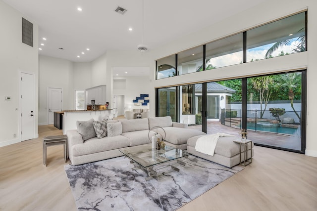 living area featuring recessed lighting, visible vents, a towering ceiling, and light wood-style flooring