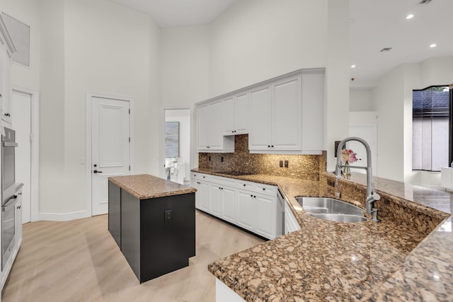 kitchen featuring backsplash, a center island, dark stone countertops, a high ceiling, and a sink