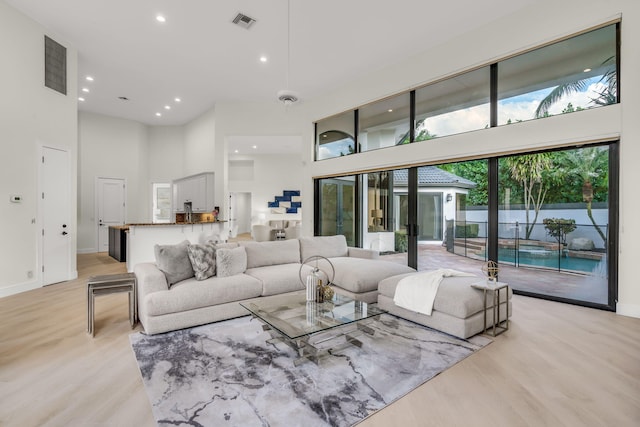 living area featuring visible vents, recessed lighting, a high ceiling, and light wood-style floors
