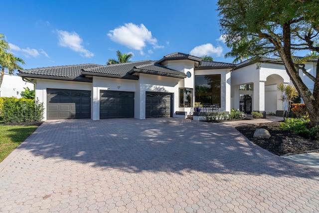 mediterranean / spanish home with decorative driveway, stucco siding, an attached garage, and a tiled roof