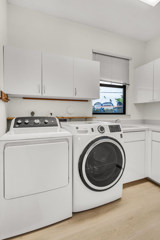 laundry room with washer and dryer, cabinet space, a sink, and light wood finished floors