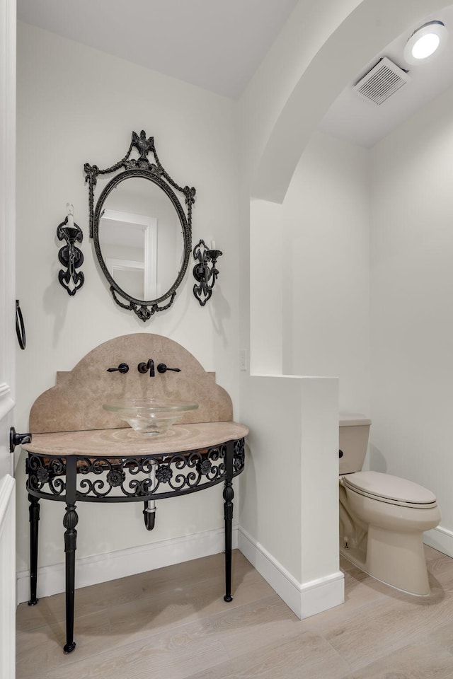 half bath featuring wood finished floors, toilet, baseboards, and visible vents