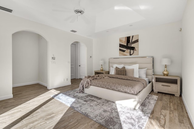 bedroom with wood finished floors, arched walkways, visible vents, and baseboards