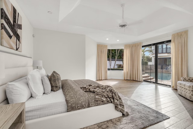 bedroom featuring a ceiling fan, access to outside, a tray ceiling, wood finished floors, and recessed lighting