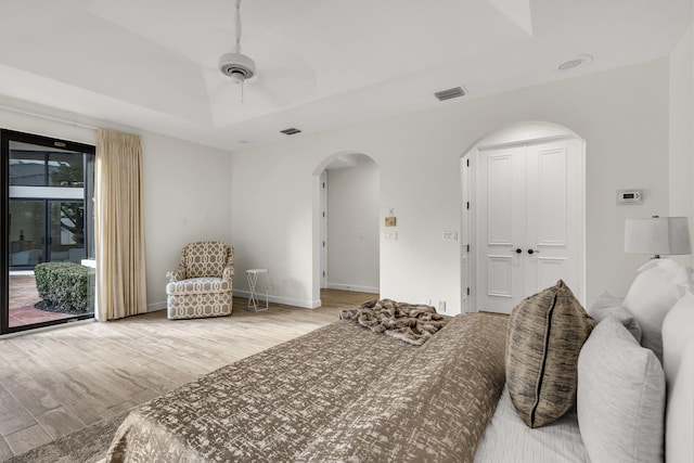 bedroom with visible vents, a tray ceiling, arched walkways, light wood finished floors, and access to exterior