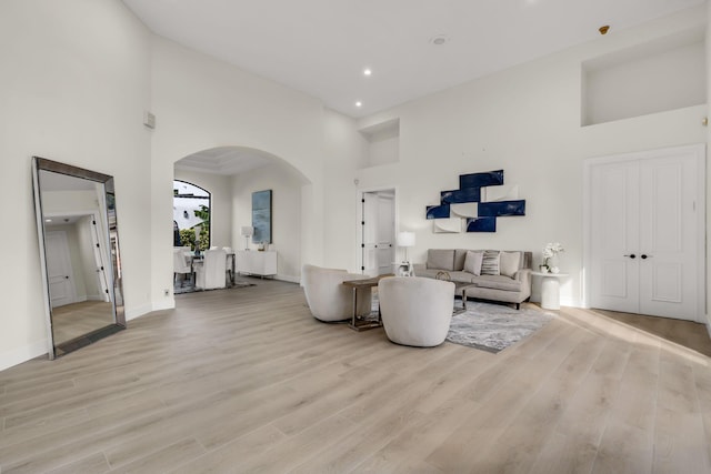 living room featuring light wood-style floors, arched walkways, a towering ceiling, and baseboards