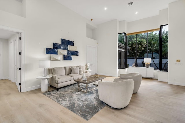 living room featuring light wood-style floors, visible vents, baseboards, and a high ceiling