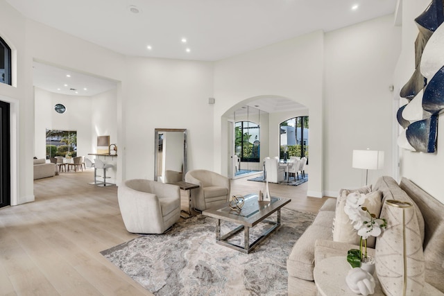 living area with wood finished floors, recessed lighting, arched walkways, baseboards, and a towering ceiling