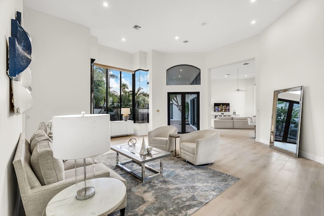 living area with light wood finished floors, visible vents, baseboards, recessed lighting, and a high ceiling