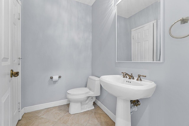 half bath with toilet, baseboards, a sink, and tile patterned floors