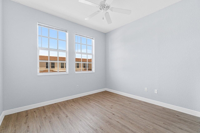 spare room featuring light wood finished floors, a ceiling fan, and baseboards
