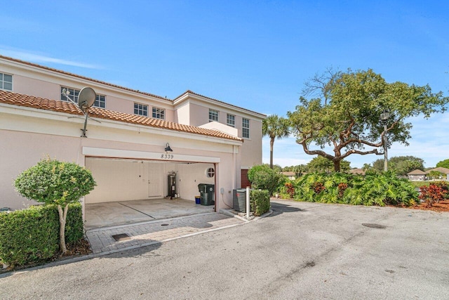 view of front of property with driveway, a garage, a tile roof, water heater, and stucco siding