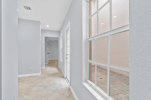 corridor with a textured wall, visible vents, and baseboards