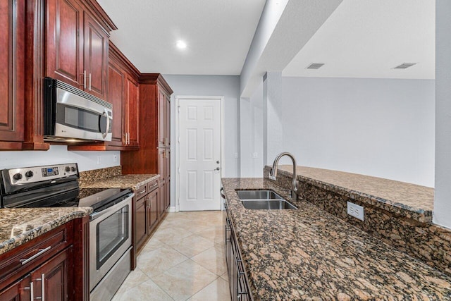 kitchen with stainless steel appliances, a sink, visible vents, dark brown cabinets, and dark stone counters