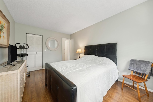 bedroom with a closet, a textured ceiling, baseboards, and wood finished floors