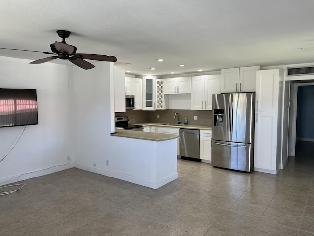 kitchen featuring visible vents, a peninsula, stainless steel appliances, white cabinetry, and a sink