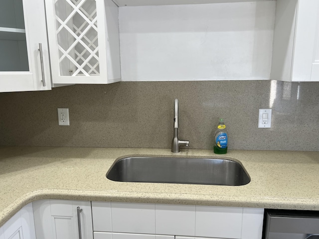 kitchen with a sink, light stone counters, dishwashing machine, white cabinets, and decorative backsplash