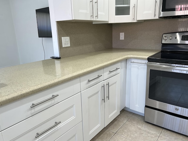 kitchen with appliances with stainless steel finishes, white cabinets, light tile patterned floors, decorative backsplash, and light stone countertops