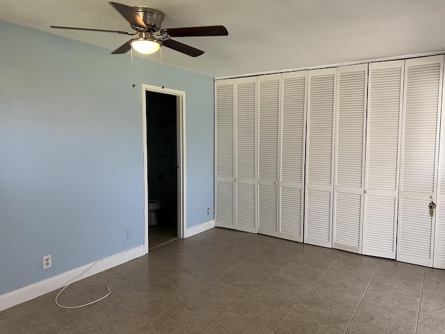 unfurnished bedroom with a closet, dark tile patterned floors, ensuite bathroom, and baseboards