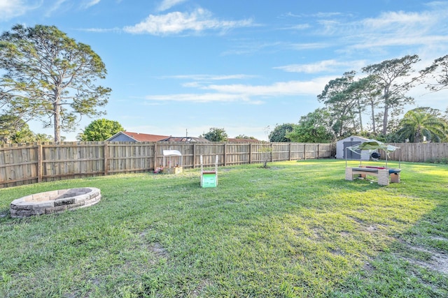 view of yard with a fenced backyard, a fire pit, and an outbuilding