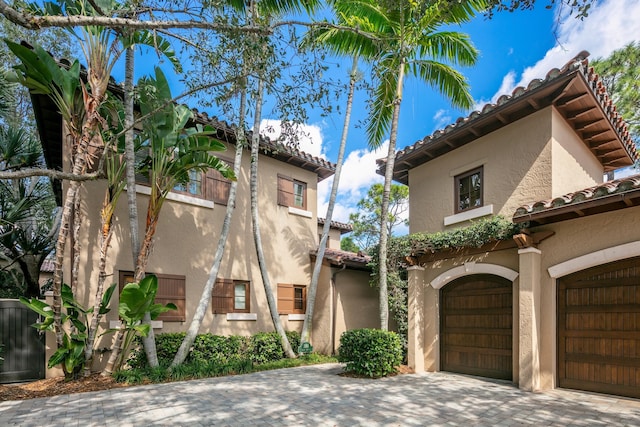 view of front facade featuring an attached garage, a tile roof, decorative driveway, and stucco siding