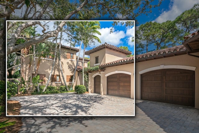 mediterranean / spanish home featuring a garage, decorative driveway, a tile roof, and stucco siding