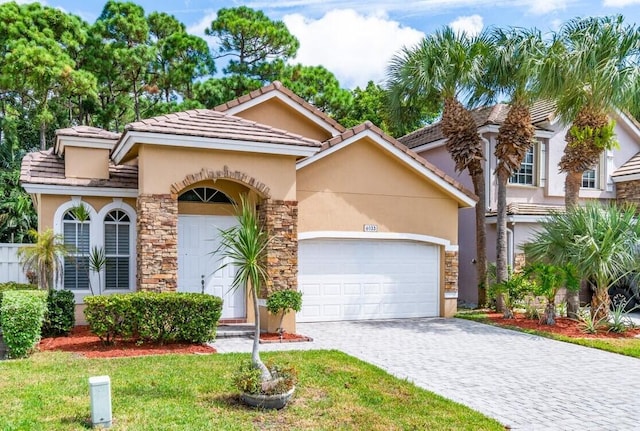 mediterranean / spanish house with stone siding, stucco siding, an attached garage, decorative driveway, and a front yard