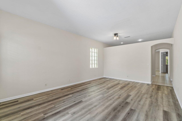 spare room featuring light wood-type flooring, baseboards, visible vents, and arched walkways