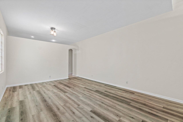 spare room featuring arched walkways, baseboards, and light wood finished floors