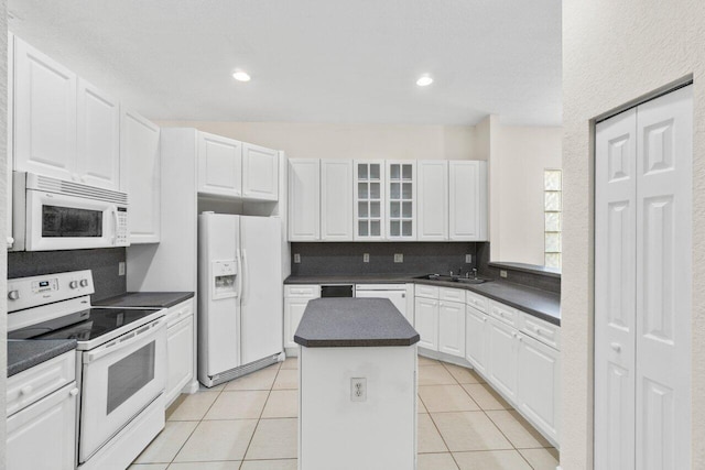 kitchen featuring light tile patterned floors, white appliances, dark countertops, and a center island