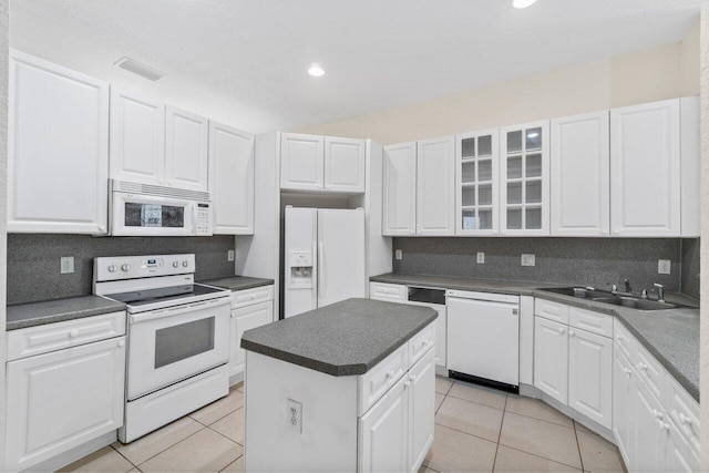 kitchen featuring light tile patterned floors, white appliances, a sink, visible vents, and dark countertops