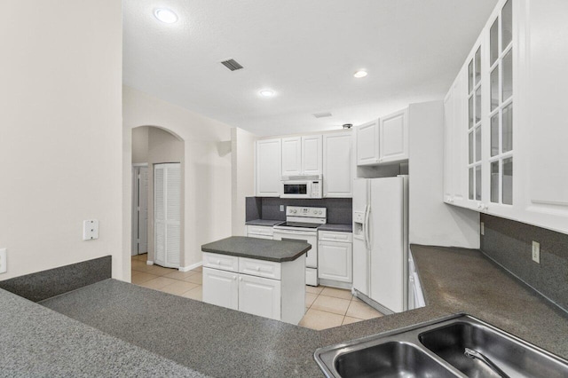 kitchen featuring white appliances, dark countertops, a sink, and visible vents