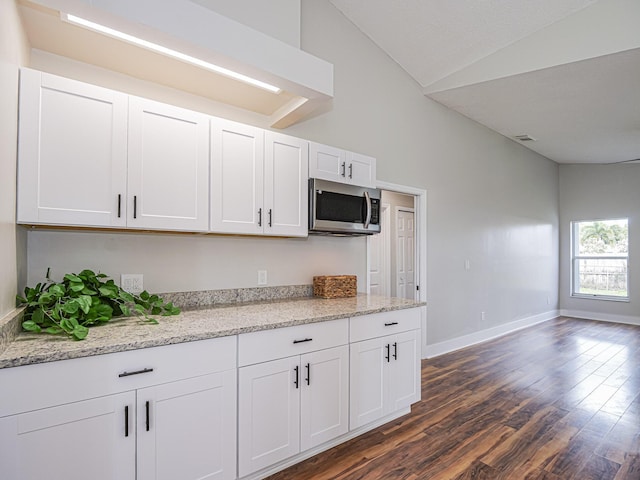 kitchen featuring dark wood-style flooring, lofted ceiling, stainless steel microwave, white cabinets, and baseboards